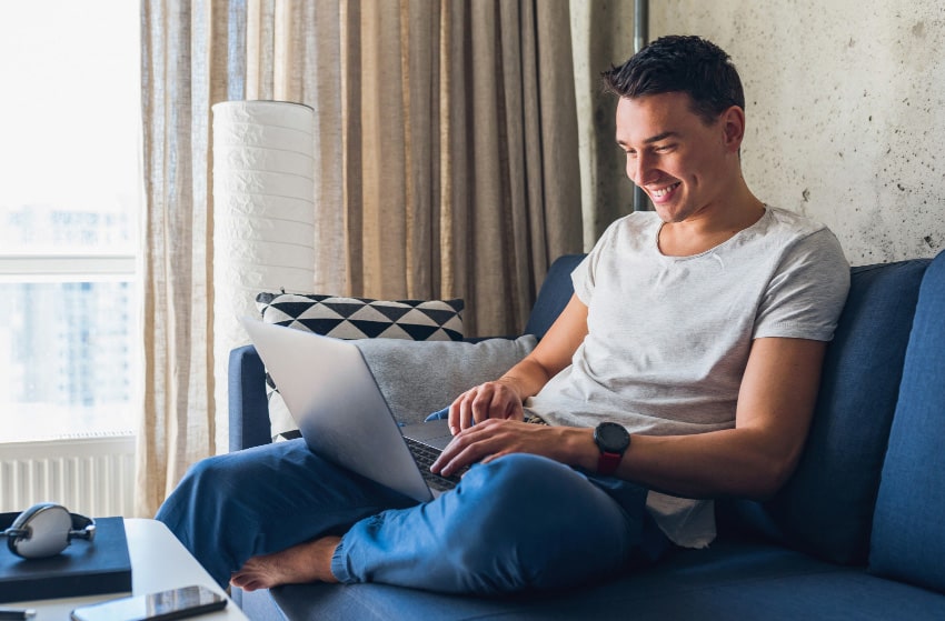young attractive man sitting sofa home working laptop online using internet min